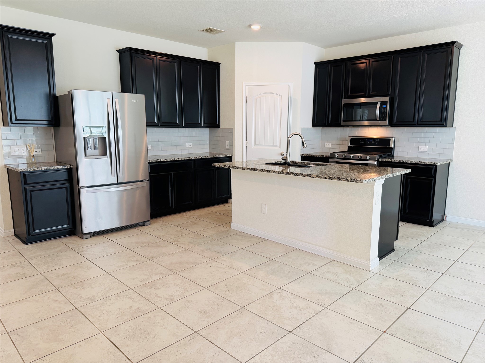 2013 Hat Bender Loop Round Rock, TX 78664 - Photo 4 of 16 Kitchen with dark cabinetry, light stone countertops, stainless steel appliances, a center island with sink, and decorative backsplash