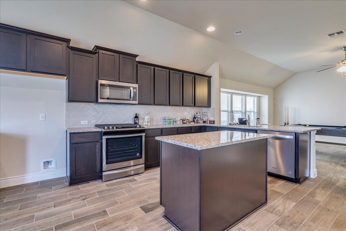 124 Compass Lane Kyle, TX 78640 - Photo 11 of 38 a kitchen with stainless steel appliances granite countertop a stove top oven a sink and dishwasher a refrigerator with wooden floor