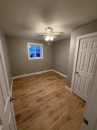 an empty room with wooden floor chandelier fan and windows