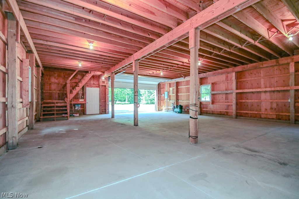 6475 Taylor Road Painesville, OH 44077 - Photo 20 of 23 Spacious 2 of 2 out building interior featuring exposed wood beams and ceiling joists, durable concrete flooring, and a visible staircase providing access to an upper level