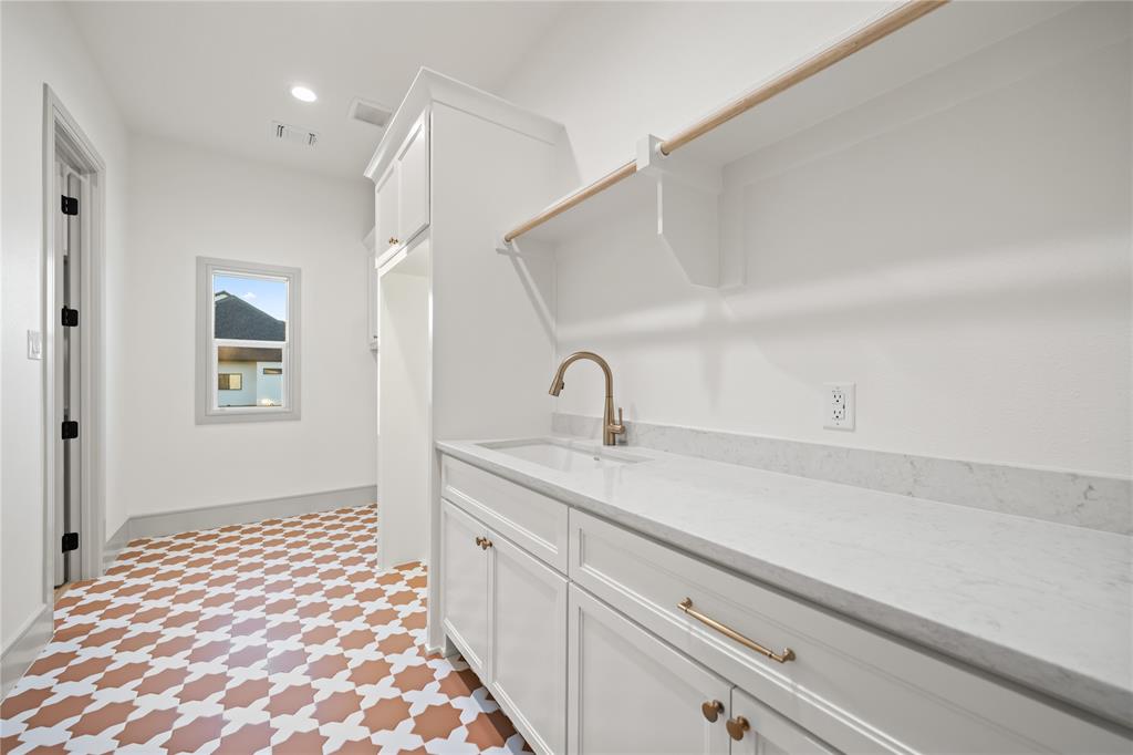 724 Cooper Trail Weatherford, TX 76087 - Photo 32 of 37 Laundry room featuring intricate patterned tile flooring, a white vanity with a rectangular undermount sink, a gold-finish faucet, white cabinetry with gold-finish hardware, and a built-in shelving unit with a hanging rod