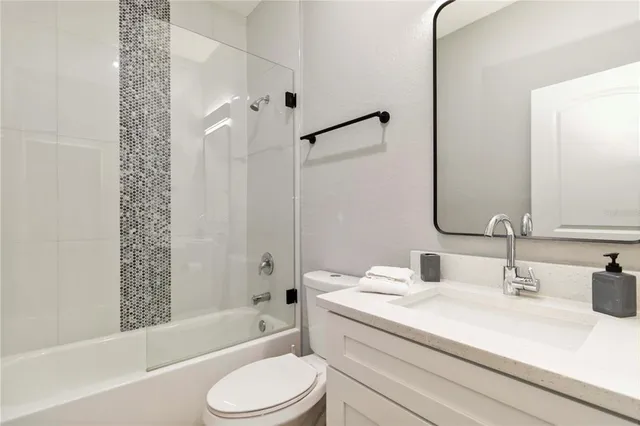 a bathroom with a granite countertop bathtub shower sink vanity mirror and toilet