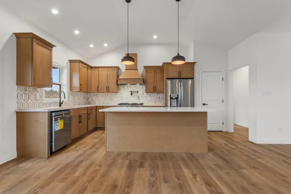 a large kitchen with granite countertop a stove a sink a refrigerator and a wooden floor