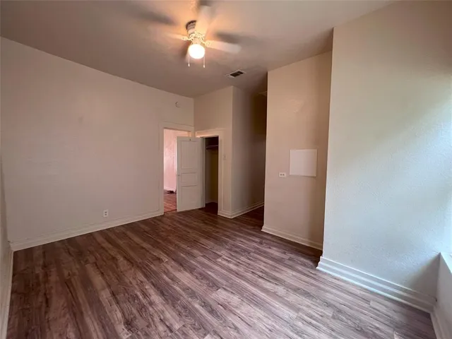 a view of an empty room with wooden floor and a ceiling fan