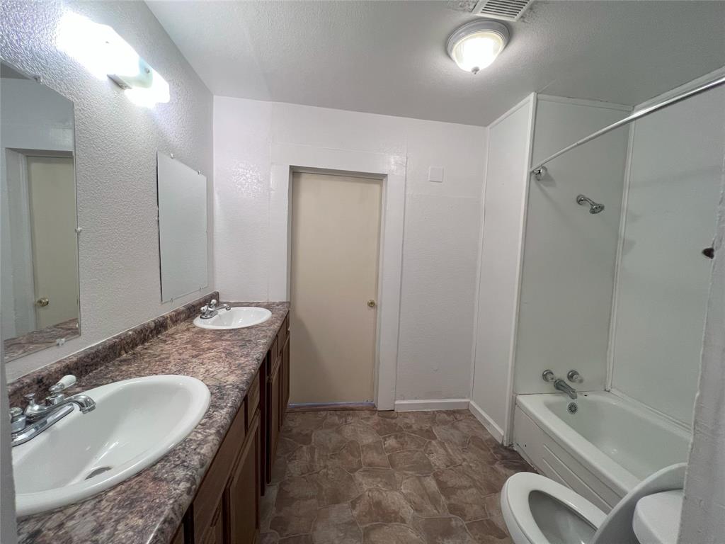 317 Ritchey Street Gainesville, TX 76240 - Photo 5 of 13 Full bathroom featuring toilet, double vanity, a sink, and bathing tub / shower combination