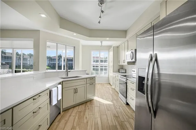 a kitchen with stainless steel appliances granite countertop a refrigerator a sink dishwasher a stove and white countertops with wooden floor