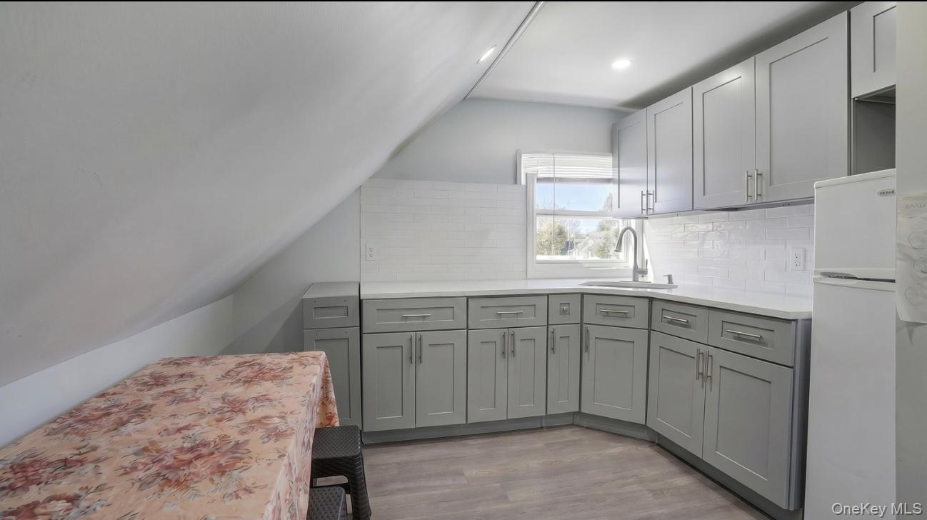 63 Blacksmith Road Levittown, NY 11756 - Photo 22 of 25 Kitchen area featuring light gray cabinetry, white countertops, a white subway tile backsplash, a stainless steel sink with a gooseneck faucet, and wood-finish flooring