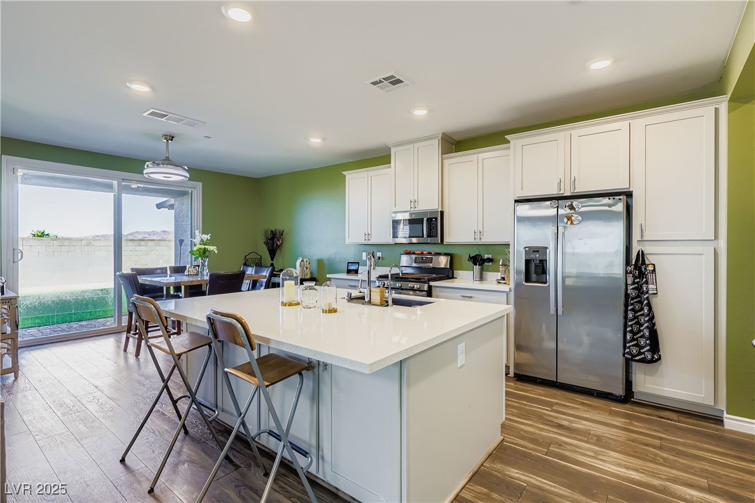 314 Robson Rdg Lane Henderson, NV 89015 - Photo 16 of 64 Kitchen with stainless steel appliances, dark wood-style flooring, a kitchen island with sink, a kitchen breakfast bar, and white cabinetry