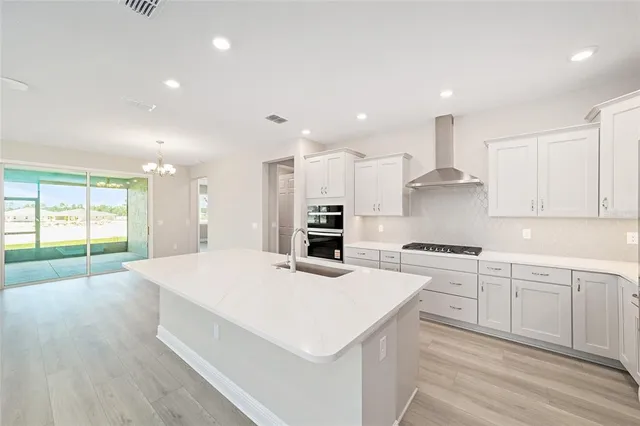 a large kitchen with kitchen island a stove a sink a refrigerator and white cabinets with wooden floor