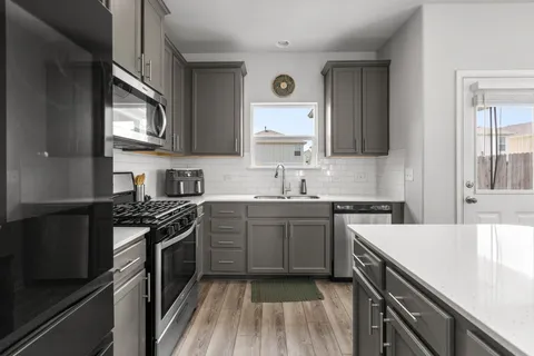a kitchen with stainless steel appliances granite countertop a stove top oven a sink dishwasher and a refrigerator with wooden floor