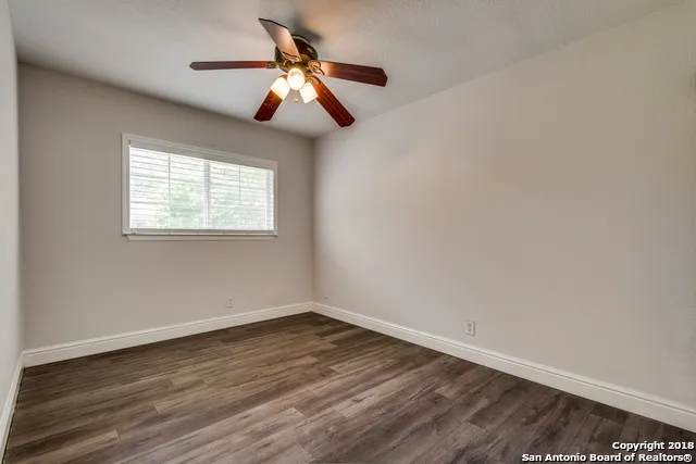 an empty room with wooden floor fan and windows