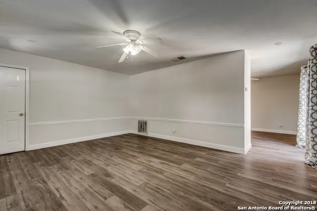a view of an empty room with wooden floor and a ceiling fan