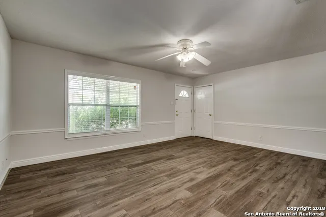 an empty room with wooden floor fan and windows