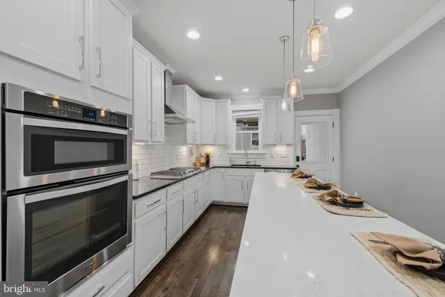 a kitchen with stainless steel appliances kitchen island granite countertop a stove top oven a sink dishwasher and a microwave oven with wooden floor