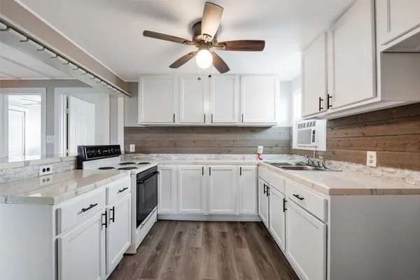 a kitchen with a sink dishwasher a stove a refrigerator with white cabinets and wooden floor