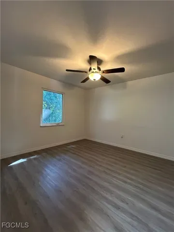 an empty room with wooden floor chandelier fan and windows