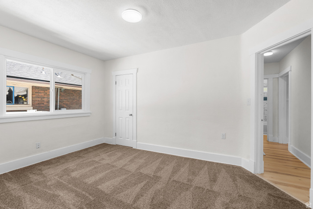 2862 Fowler Avenue Ogden, UT 84403 - Photo 12 of 23 Spacious room featuring new carpet, crisp white walls, a large window with white trim, a solid door with white trim, and a ceiling-mounted light fixture