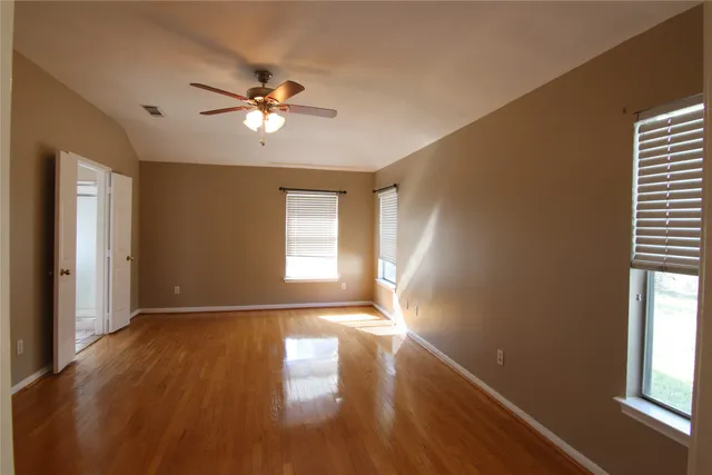 a view of empty room with wooden floor and fan