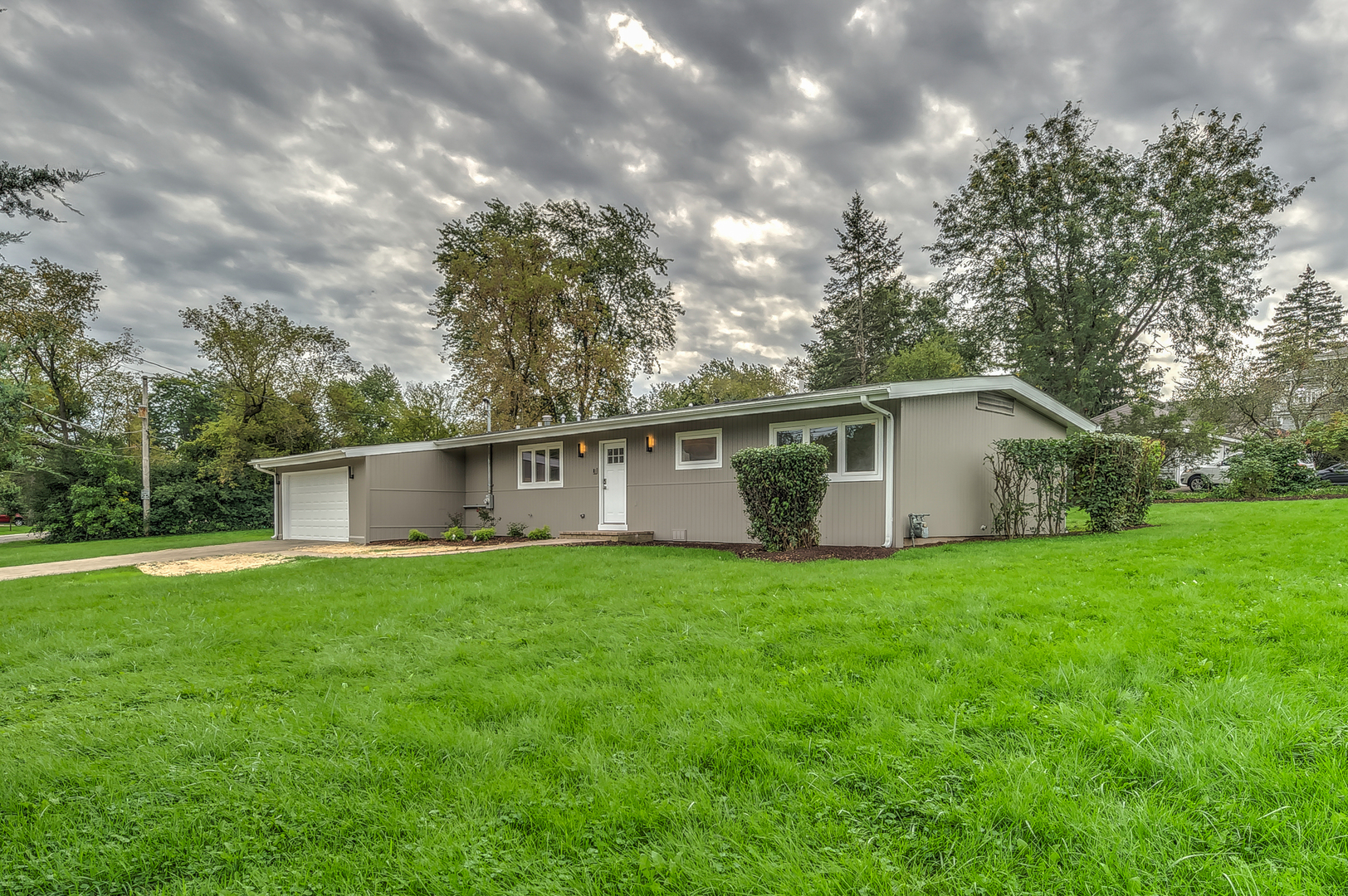 a house that is sitting in the grass with large trees and plants