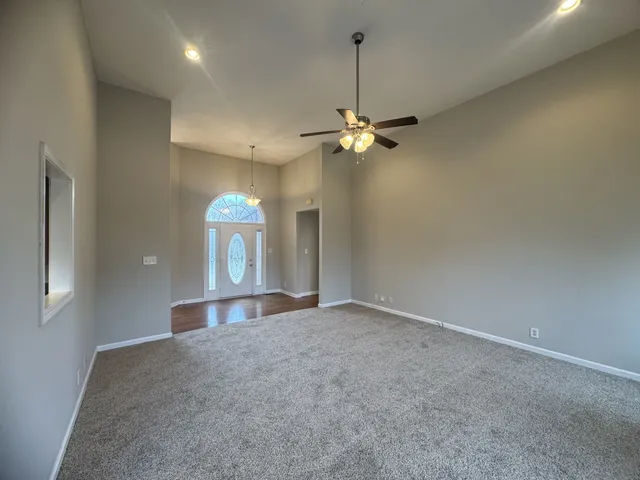 an empty room with chandelier fan and windows
