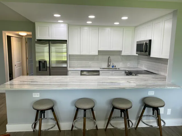 a kitchen with stainless steel appliances granite countertop a sink a stove a refrigerator and white cabinets with wooden floor