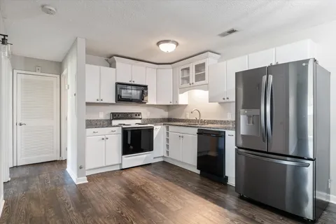 a kitchen with granite countertop white cabinets a refrigerator and a sink