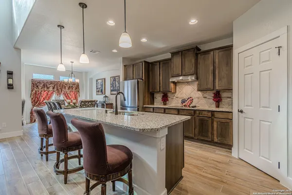a kitchen with stainless steel appliances granite countertop a stove a refrigerator a kitchen island a dining table and chairs with wooden floor