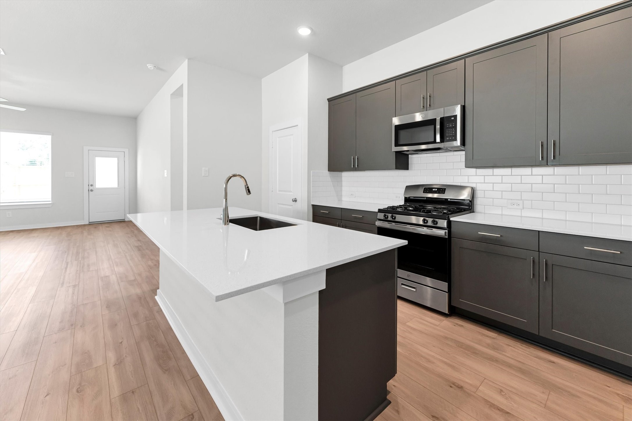 16931 Tulip Row Lane Cypress, TX 77429 - Photo 15 of 48 Modern kitchen with large eat-in island, dark cabinets, white subway tile backsplash, stainless steel appliances, and sleek quartz countertops.