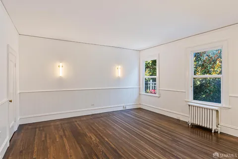 an empty room with wooden floor fireplace and windows