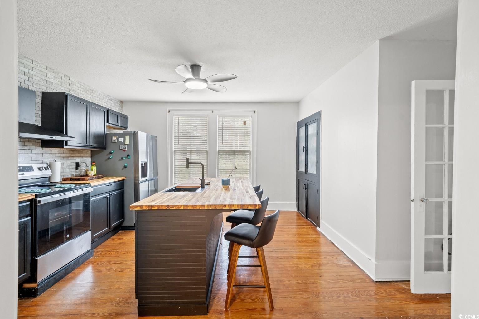 222 East Wine Street Mullins, SC 29574 - Photo 14 of 40 Kitchen with wooden counters, a kitchen bar, stainless steel appliances, light wood-type flooring, and a textured ceiling