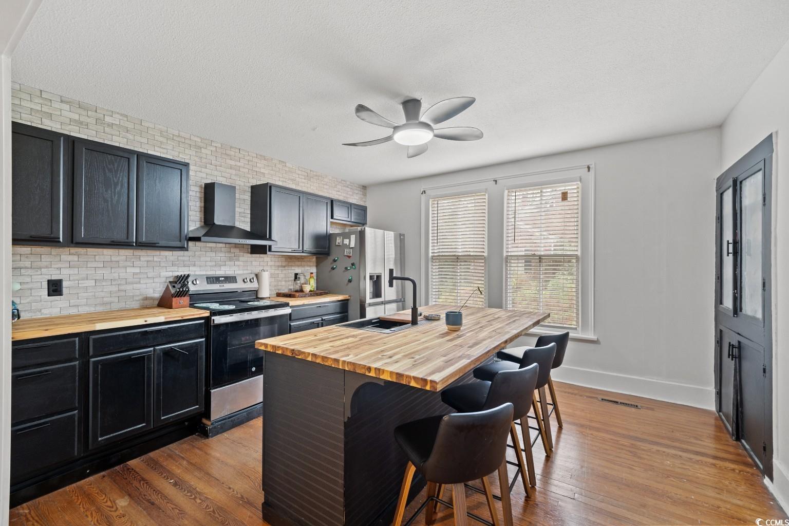 222 East Wine Street Mullins, SC 29574 - Photo 16 of 40 Kitchen with appliances with stainless steel finishes, dark wood-style floors, wall chimney exhaust hood, wood counters, and a kitchen bar