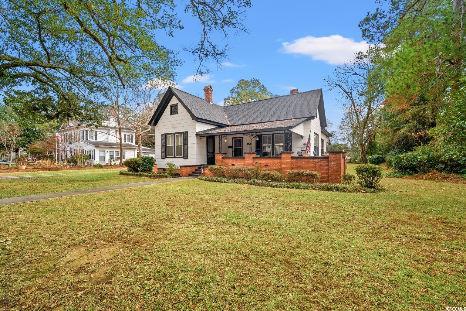 222 East Wine Street Mullins, SC 29574 - Photo 2 of 40 View of front of property featuring a front lawn, a chimney, brick siding, roof with shingles, and a porch