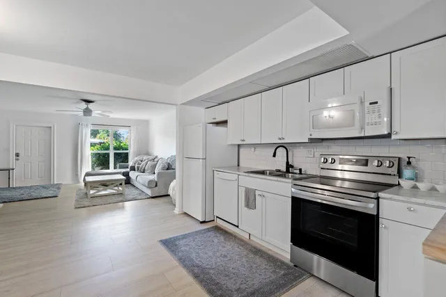 a kitchen with stainless steel appliances white cabinets a sink dishwasher a stove and a refrigerator with wooden floor