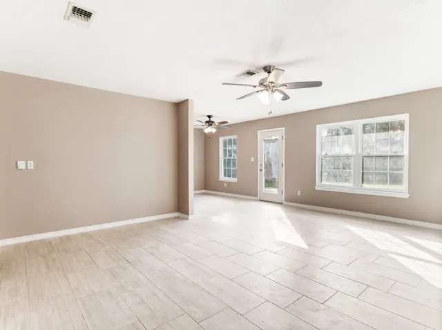 an empty room with chandelier fan and windows