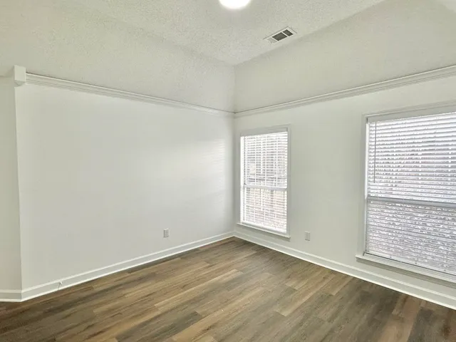 an empty room with wooden floor and windows with curtains