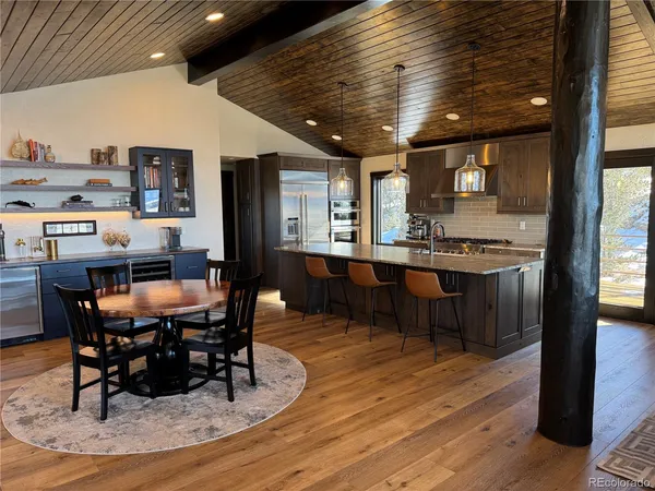 a dining hall with stainless steel appliances kitchen island granite countertop a table chairs and a wooden floor
