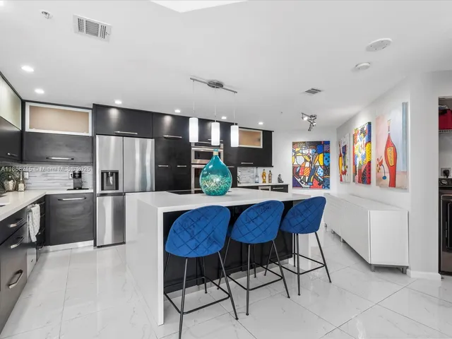 a kitchen with stainless steel appliances kitchen island granite countertop a refrigerator a stove a sink dishwasher and white cabinets with wooden floor