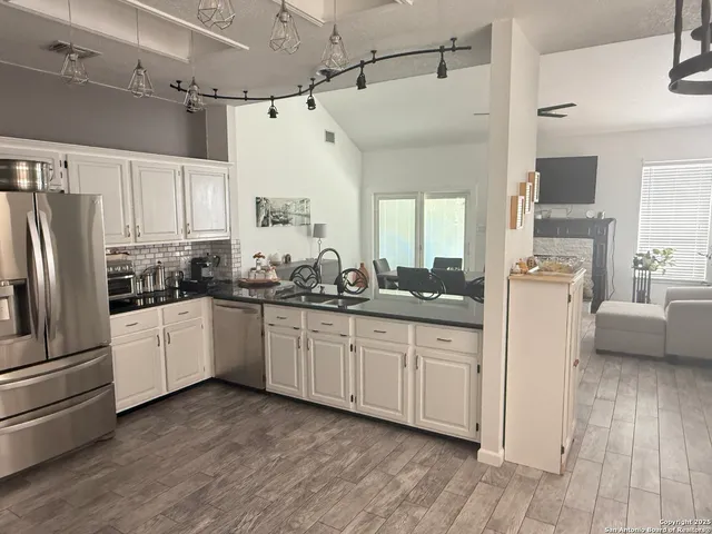 a kitchen with granite countertop a refrigerator a sink and white cabinets
