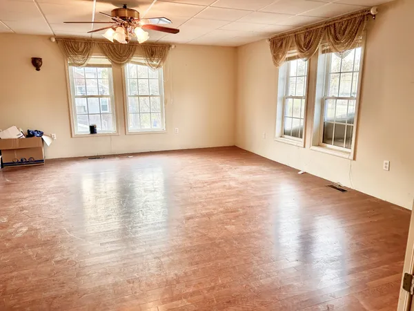 an empty room with wooden floor chandelier fan and windows