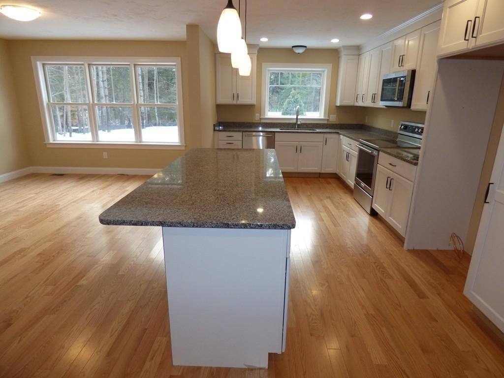 16 Kevin's Way, Unit 7 Scituate, MA 02066 - Photo 3 of 19 a kitchen with granite countertop a stove a sink a refrigerator and white cabinets with wooden floor