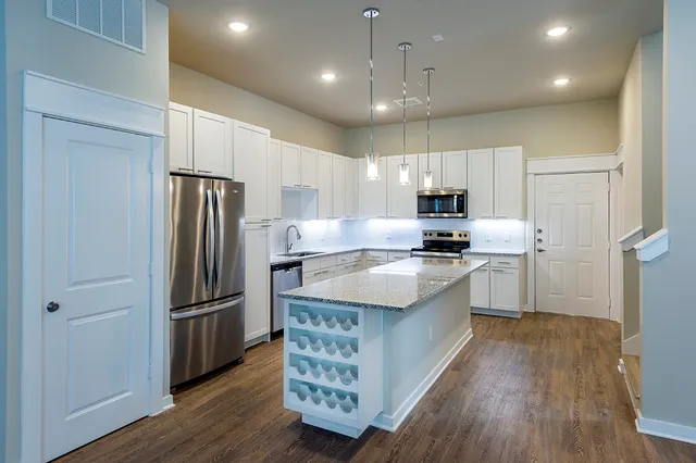 a large kitchen with stainless steel appliances granite countertop a refrigerator stove a sink and white cabinets with wooden floor