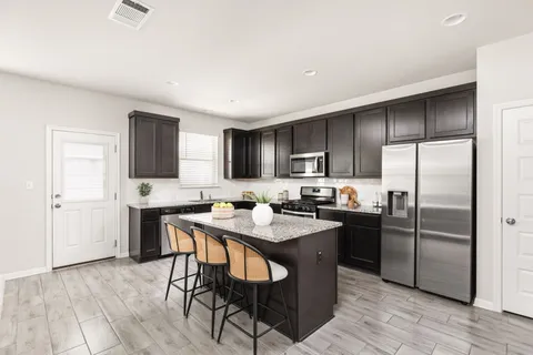 a kitchen with stainless steel appliances granite countertop a refrigerator a sink a stove a dining table and chairs