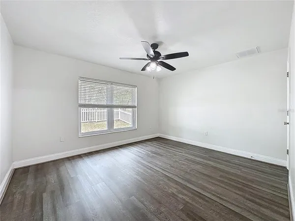 an empty room with wooden floor fan and windows