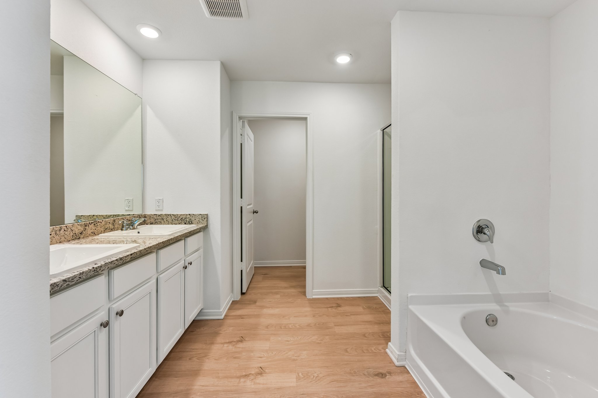 346 Low Pasture Trail Maxwell, TX 78656 - Photo 21 of 29 Bathroom featuring wood-finish flooring, a double vanity with stone-finish countertop and undermount sinks, a built-in bathtub with polished chrome fixtures, and a glass-enclosed shower