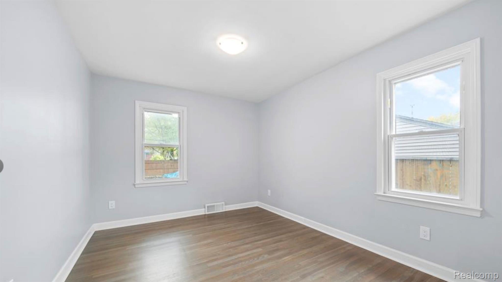 4214 Berkshire Road Royal Oak, MI 48073 - Photo 13 of 27 Bright interior space featuring two white-framed windows, wood-finish flooring, light gray walls, white baseboards, and a ceiling-mounted light fixture