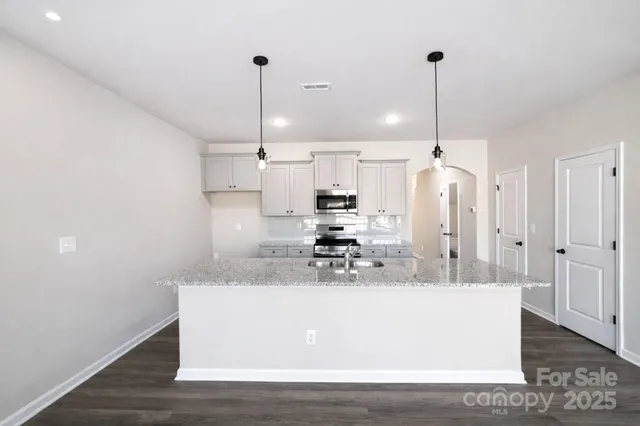 a view of a kitchen with stainless steel appliances granite countertop a sink a refrigerator and a wooden floor