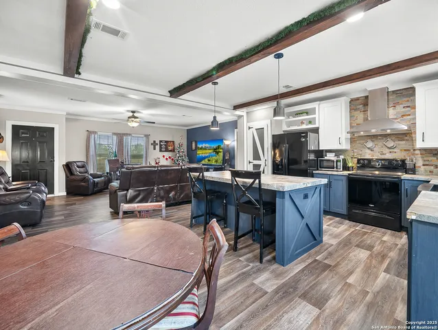 a kitchen with stainless steel appliances kitchen island granite countertop a refrigerator a stove a sink a dining table and chairs with wooden floor