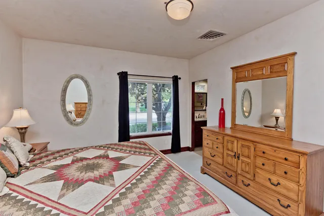 a bedroom with a bed a mirror on dresser and a large window