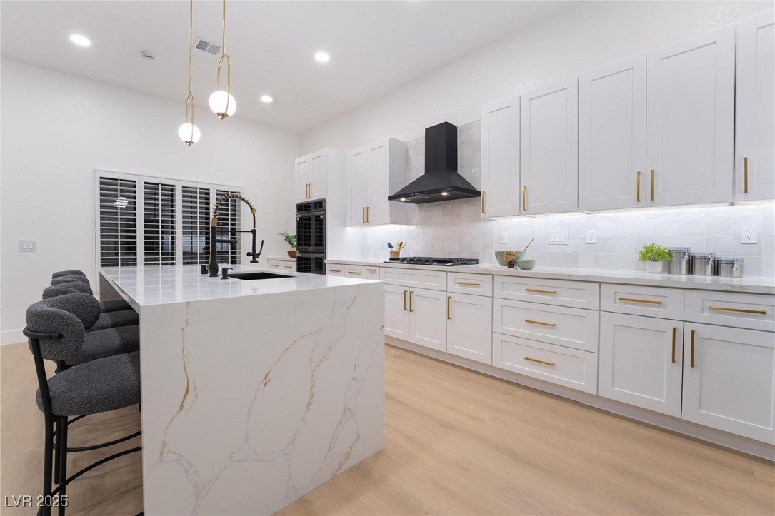 2528 Sunup Drive Las Vegas, NV 89134 - Photo 9 of 24 Kitchen featuring tasteful backsplash, hanging light fixtures, a breakfast bar area, light wood-type flooring, and light stone counters