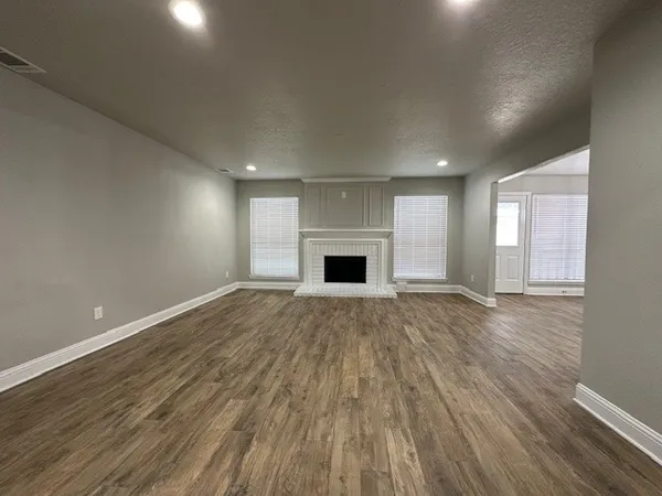 an empty room with wooden floor fireplace and windows